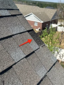 Asphalt shingle roof with red arrow pointing to a dark, potentially wet or damaged section.
